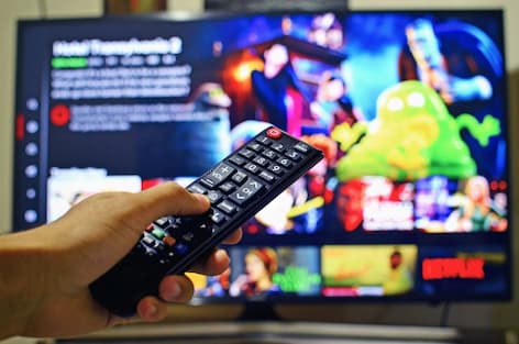 Hand holding remote control while watching Netflix on TV, featuring animated movie scene.
